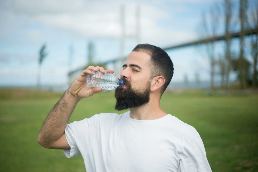 A man is drinking water while standing in the sports ground.