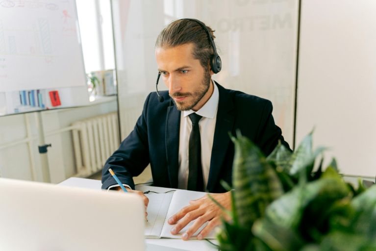 A man in a suit and tie is seated at a desk, working on a laptop with a focused expression. Which is one of the important aspect of communication skills.