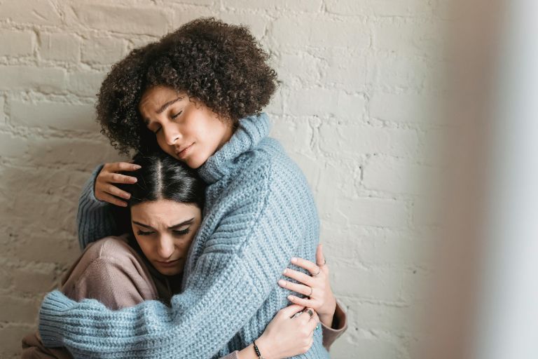 A heartfelt hug between two women against a rustic brick wall, symbolizing support and camaraderie.