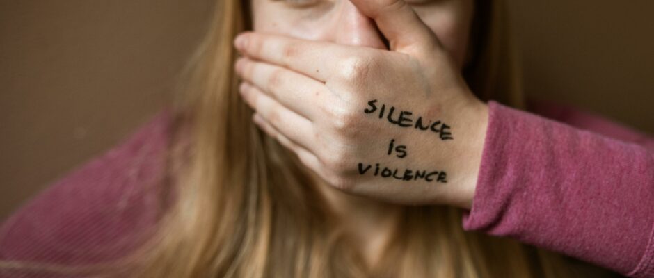 A girl having hand on this mouth with the text Silence is Violence.