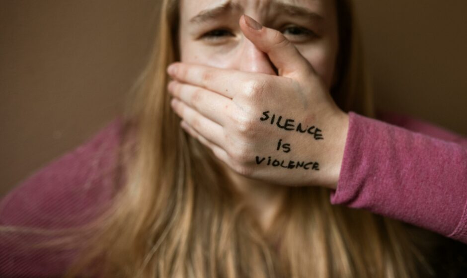 A girl having hand on this mouth with the text Silence is Violence.