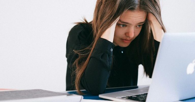 A girl is in stress while staring at the screen of the laptop. which is the indication of a week Emotional Intelligence.